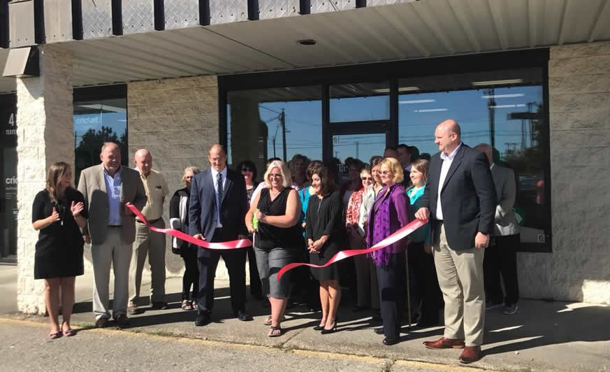 A group of people outside the Teays Valley Office and the owner is cutting a ribbon